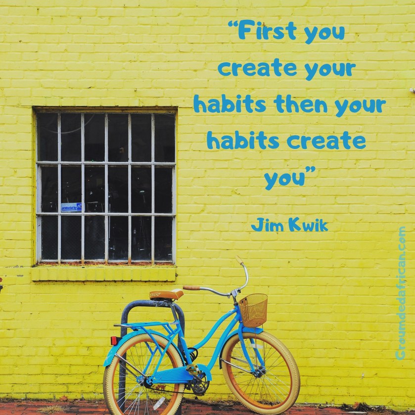 Blue ladies bicycle resting on bike post in front of a bright yellow wall and large window