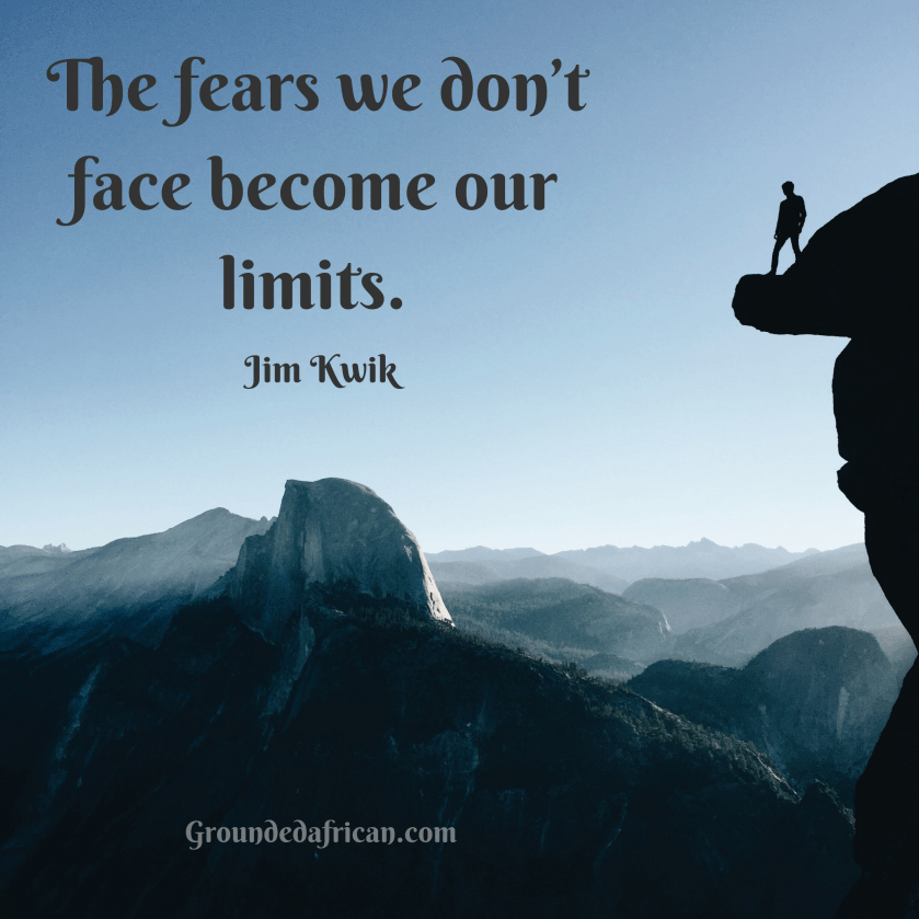 Man on mountain ledge overlooking mist laden hills. 